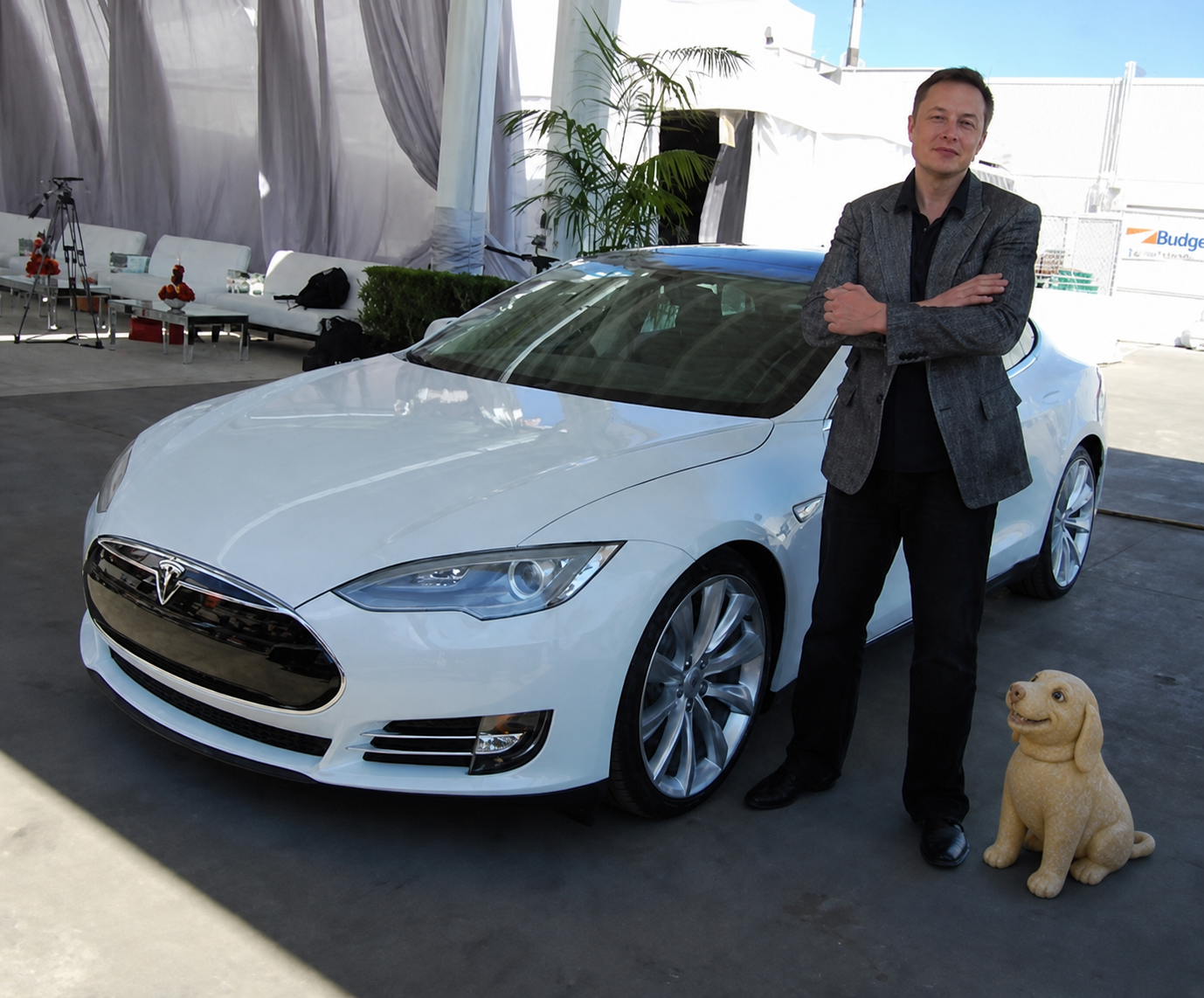 Elon Musk standing beside a white Tesla with Dough Dog